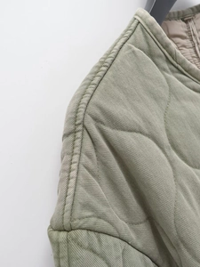 Détails macro de la veste matelassée vert olive avec surpiqûres en losange et finitions de l'ourlet