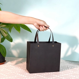 Detail of a minimalist black paper gift bag with flat handles and golden metal rivets