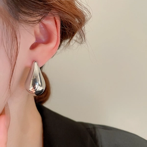 Close-up of minimalist silver teardrop earrings worn by a model with a sleek metallic finish