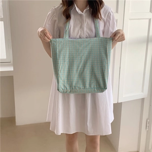 Detalle de un bolso tote de lona a cuadros azules y amarillos sostenido por una modelo