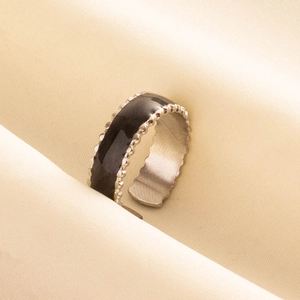 Détail d'une bague ouverte en émail noir avec bords perlés argentés sur tissu beige