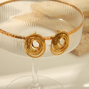 Détail de boucles d'oreilles spirales dorées superposées sur un bord en verre