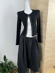 Detail view of black knit cardigan with white base shirt and long pleated skirt set