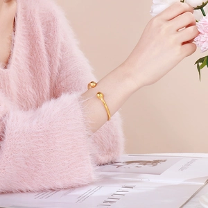 Minimalist gold ball open bangle bracelet shown on a model wearing a pink sweater
