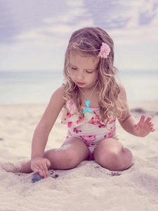 Détail du collier pendentif queue de sirène bleu dégradé sur un enfant à la plage