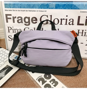 Detail of lavender nylon crossbody bag with black zipper pull and orange brand label