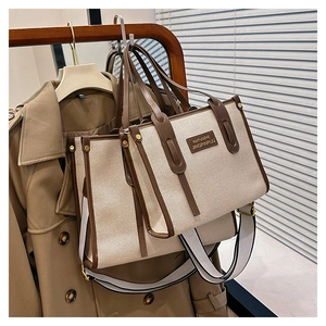 Two beige canvas tote bags with brown leather trim hanging on a wooden hanger with strap