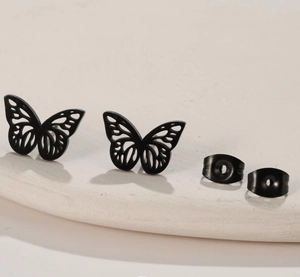 Macro detail of black hollow butterfly stud earrings with wings on a textured surface