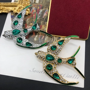 Détail de broches hirondelles avec cristaux émeraude et diamants sur fond vintage
