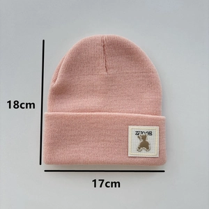 Pink knit beanie for children featuring bear patch and detailed size dimensions