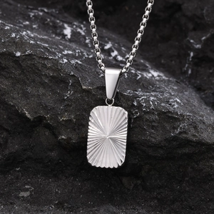 Macro shot of silver stainless steel geometric pendant with sunburst texture on dark stone