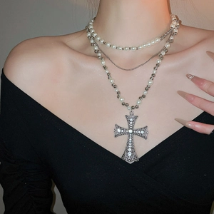 Close-up of layered pearl necklace with a large rhinestone cross pendant on a model