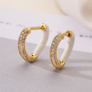 Close-up of golden heart earrings with white enamel finish and small sparkling gems