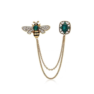 Vintage gold bee brooch with emerald rhinestones and hanging chains on white backdrop