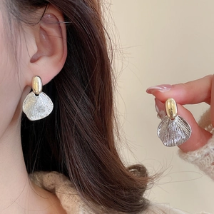 Detailed close-up of shell-shaped metal earrings with sunburst texture worn by a model