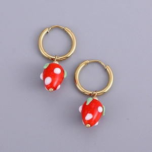 Detail view of gold hoop earrings with red strawberry pendants and glossy enamel finish