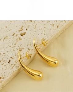 Macro detail of gold teardrop earrings with high-polish mirror finish on stone surface