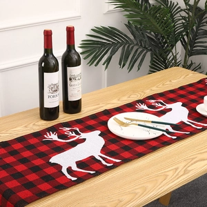 Red and black plaid Christmas table runner with white reindeer pattern on wooden table