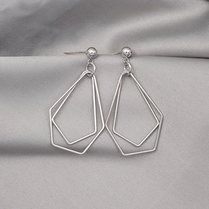 Macro shot of silver geometric double pentagon drop earrings on silk background