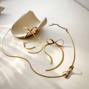 Macro shot of gold bow knot long fringe earrings and snake chain necklace set