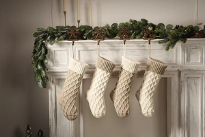 Details von vier beige und khakifarbenen gestrickten Weihnachtssocken am Kamin