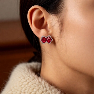 Detailed close-up of bow-shaped ear clip with red heart-shaped stones and white crystals