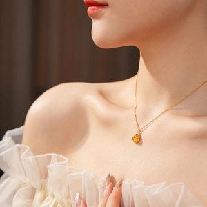 Close-up of gold-plated Buddha pendant necklace with amber-tone gemstone on model neck