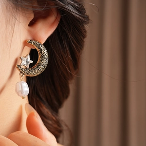 Close-up of vintage gold crescent moon earring with star gem and dangling white pearl