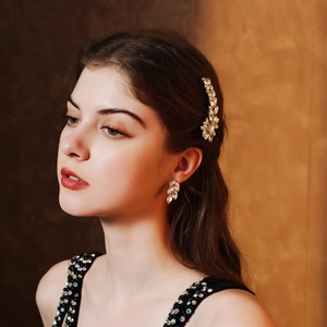 Detail of elegant gold metal hair clip and earrings with crystal leaf design on a model