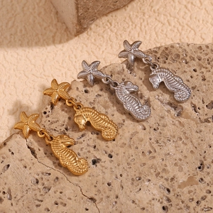 Macro shot of 18K gold and silver seahorse starfish earrings on natural stone