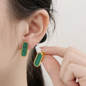 Close-up of a gold oval earring featuring a green malachite inlay worn by a model
