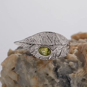 Macro shot of silver leaf pendant with green garnet stone on a natural stone surface