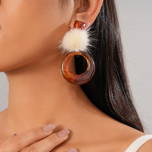 Detail of amber resin drop earrings with cream faux fur pom pom on model