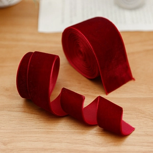 Luxurious burgundy velvet Christmas ribbon with white stitched edges on wood surface