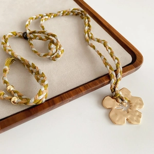 Detail of woven rope necklace with gold flower pendant on beige velvet jewelry tray