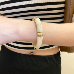 Detail of cream acrylic geometric bangle with polished gold metal links on a model's wrist
