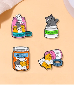 Set of four colorful cartoon cat enamel pins with Happy Pills text on orange background
