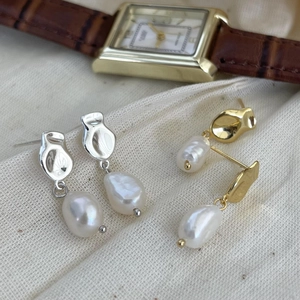 Detailed shot of irregular baroque pearl earrings in gold and silver on textured fabric