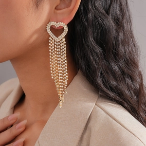 Close-up of gold heart drop earrings with long rhinestone tassels worn by a model