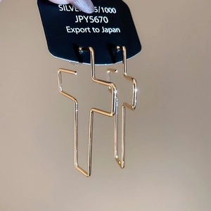 Détail de boucles d'oreilles croix géométriques dorées sur carte avec poinçon argent S925