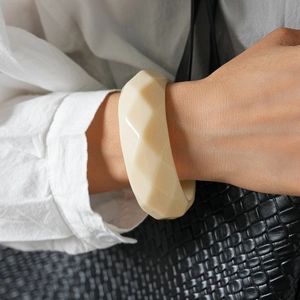 Makro-Detail eines cremefarbenen Acryl-Armreifs am Handgelenk mit Leinen-Styling