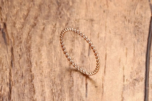 Nahaufnahme eines minimalistischen Roségold-Rings mit gedrehter Textur auf Holzgrund