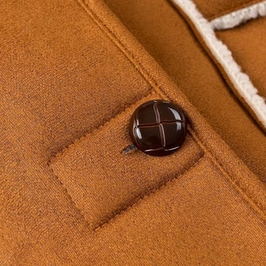 Detailed macro view of a dark brown round button on a suede jacket with shearling lining