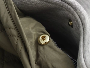 Detailed close-up of golden metal snaps on olive green quilted jacket fabric