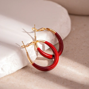Detail of red enamel and gold circle earrings on a textured stone surface display
