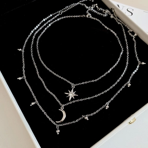 Detail of silver layered necklace with rhinestone star and moon charms on black velvet