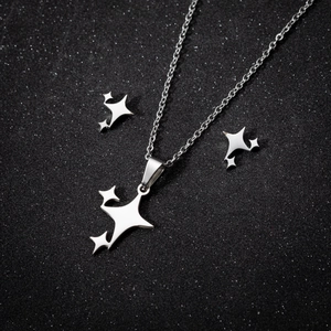 Silbernes Edelstahl-Schmuckset mit Sternanhängern auf schwarzem Glitzer-Hintergrund