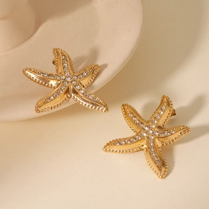 Close-up of golden starfish earrings with white rhinestones on ceramic plate