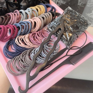 Flat lay of colorful scrunchies, black elastic bands, and a styling comb on a pink tray