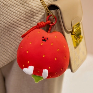 Cute plush strawberry pendant with yellow seeds and white heart feet on a beige handbag